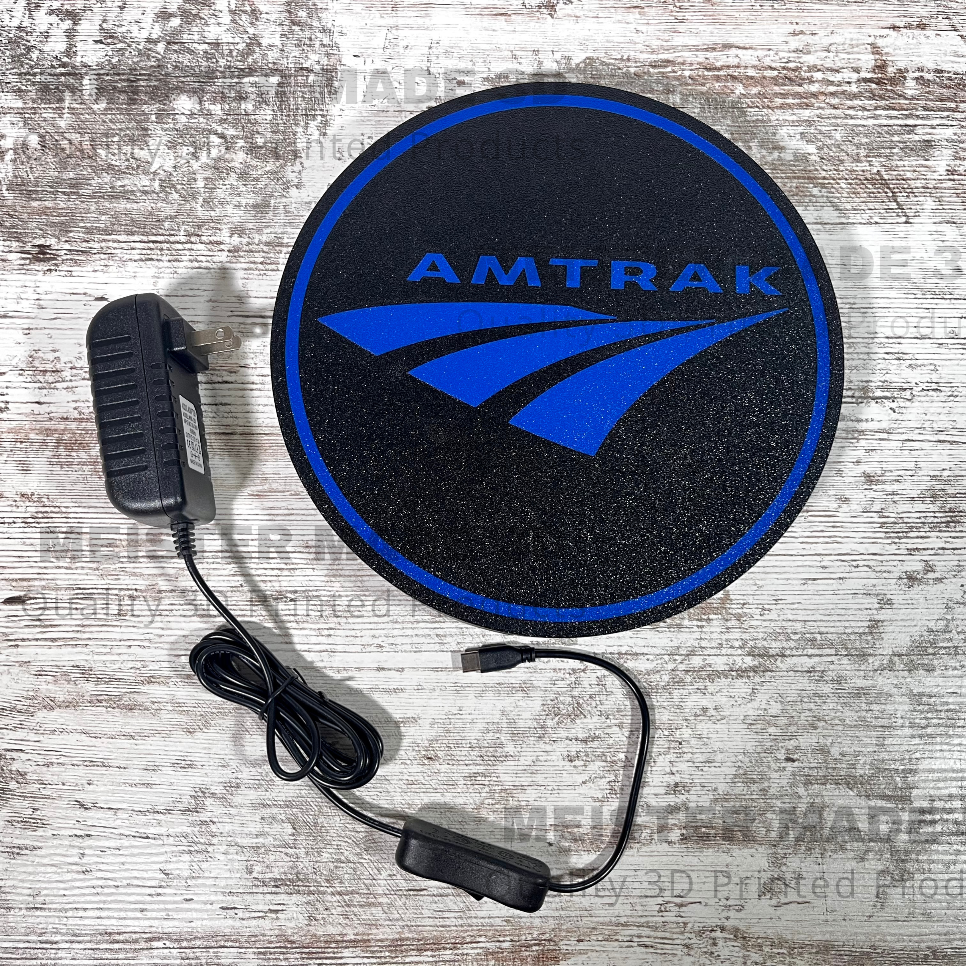 Amtrak LED light up sign with a black powersupply beside it that has a on/off switch and usb-c connector all on a wood background