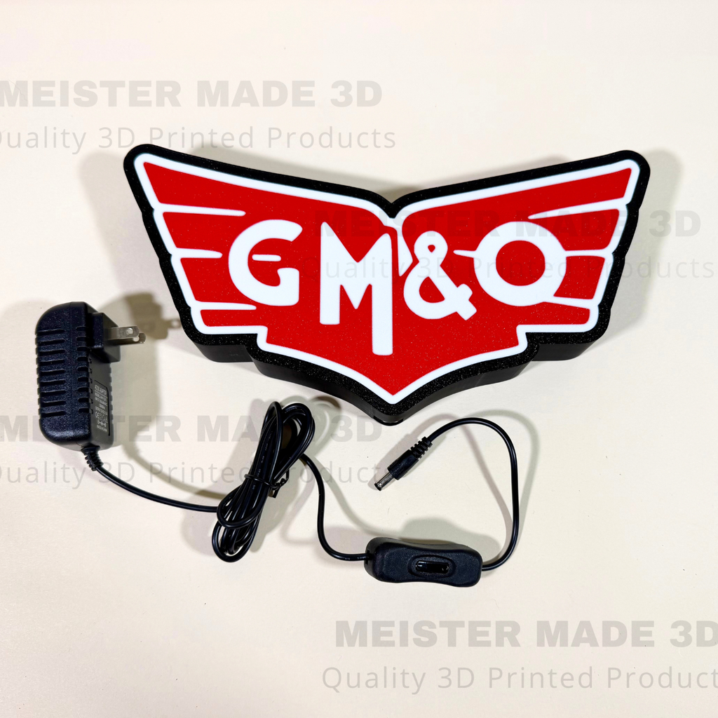A red, white, and black GM&O wing-shaped LED light sign with its power adapter and wiring, displayed on a light beige background with watermarks.