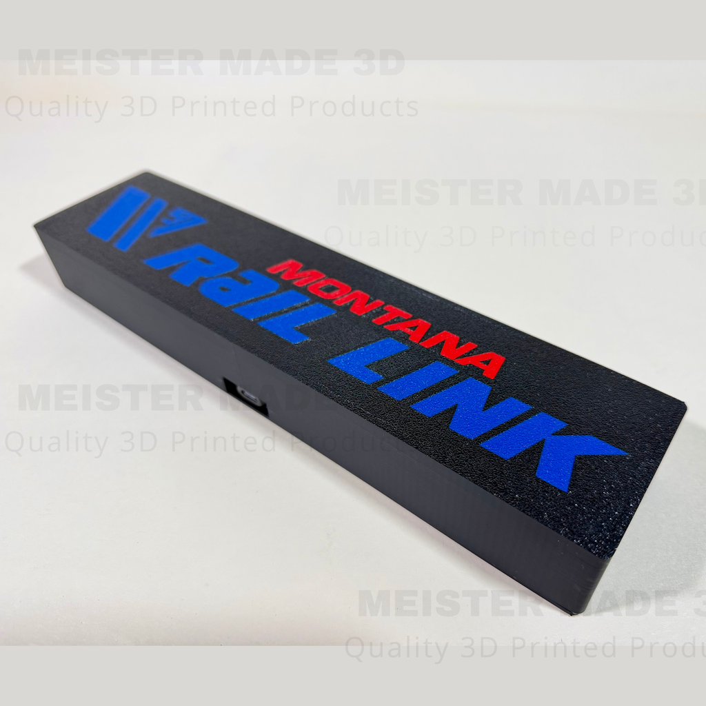 Angled view of Montana Rail Link illuminated sign showing textured black finish and raised blue and red lettering.
