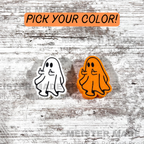 Two ghost-shaped stanley buddies, one white and one orange, on a textured wooden background with 'Pick Your Color!' text.