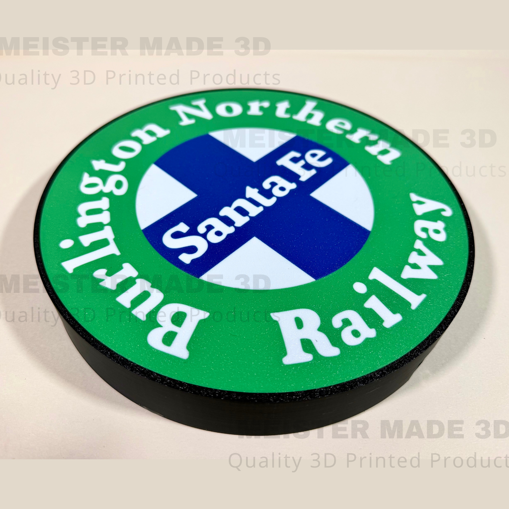 A circular 3D-printed sign featuring the Burlington Northern Santa Fe Railway logo, with a green outer ring, white lettering, a blue and white cross in the center, and a black raised edge, shown on a light beige background with faint watermarks.