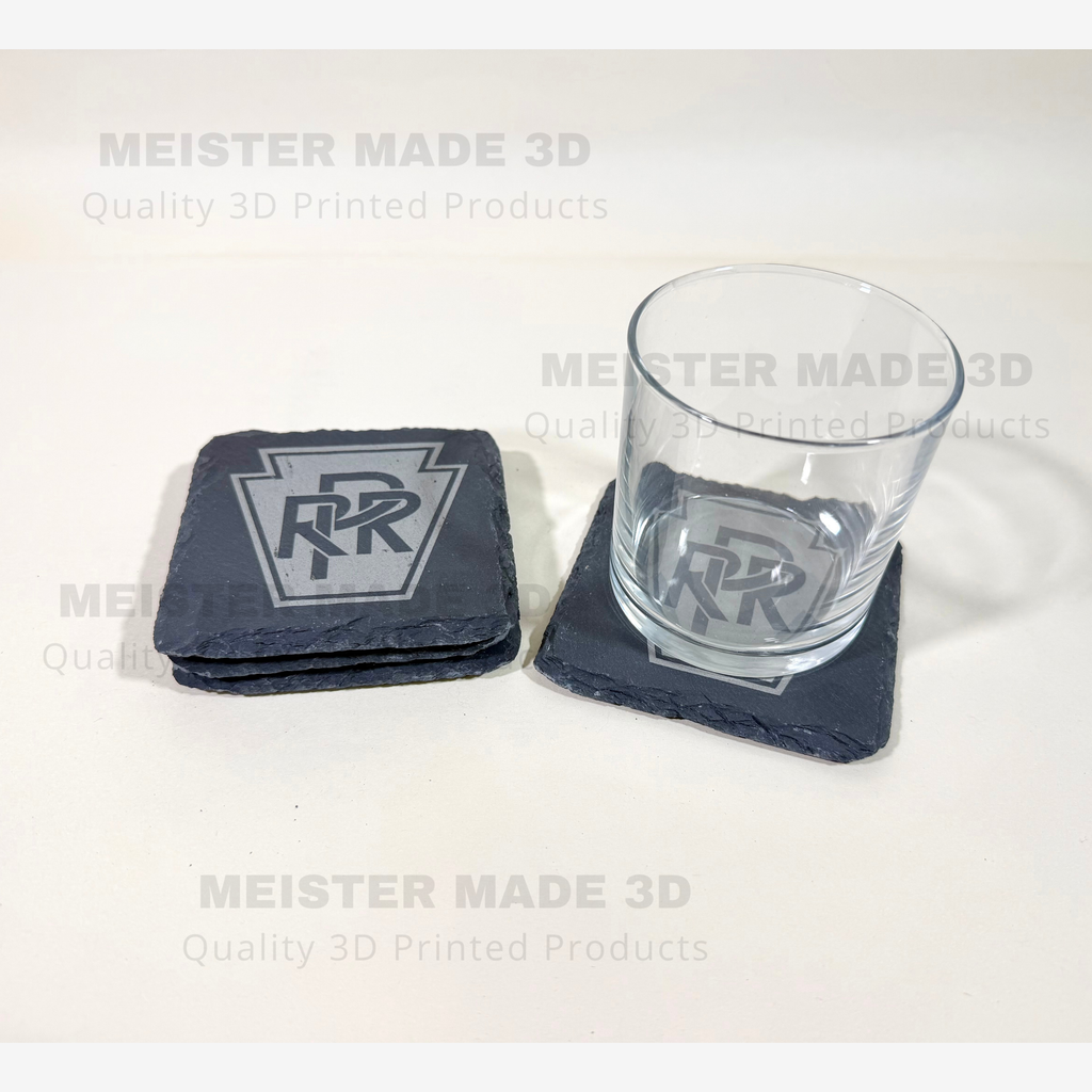 Pennsylvania Railroad PRR slate coaster shown with a drinking glass, featuring the engraved PRR keystone logo and natural black slate finish.