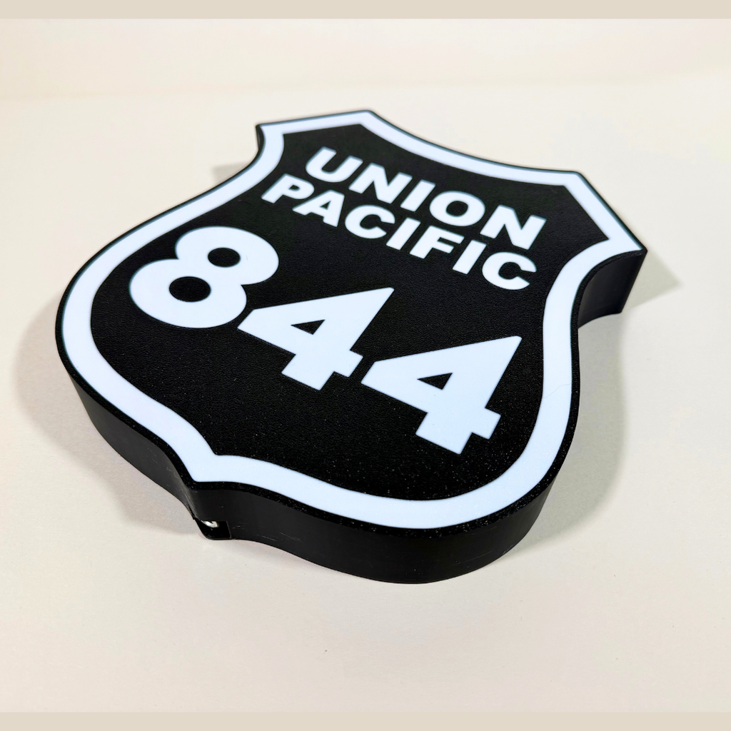 Angled close-up of a Union Pacific 844 railroad shield LED sign, featuring a black background, white lettering, and illuminated white border in a 3D printed design.