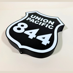 Angled close-up of a Union Pacific 844 railroad shield LED sign, featuring a black background, white lettering, and illuminated white border in a 3D printed design.
