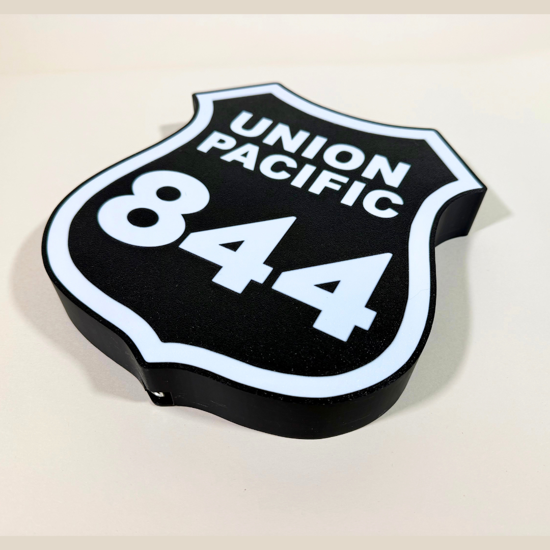 Angled close-up of a Union Pacific 844 railroad shield LED sign, featuring a black background, white lettering, and illuminated white border in a 3D printed design.