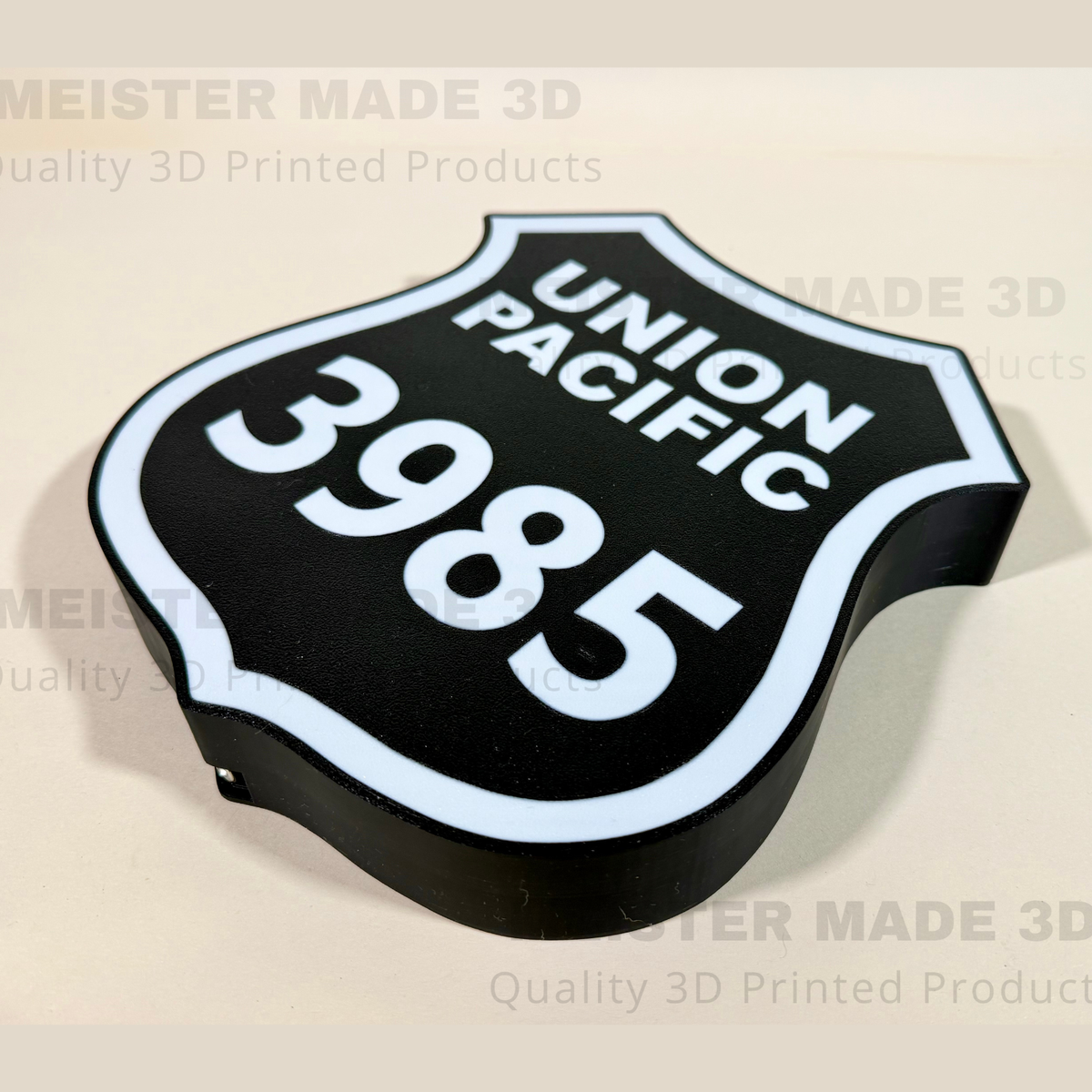 A 3D printed black shield-shaped sign with white lettering reading 'UNION PACIFIC' and the number '3985', shown on a light beige background with watermarks.