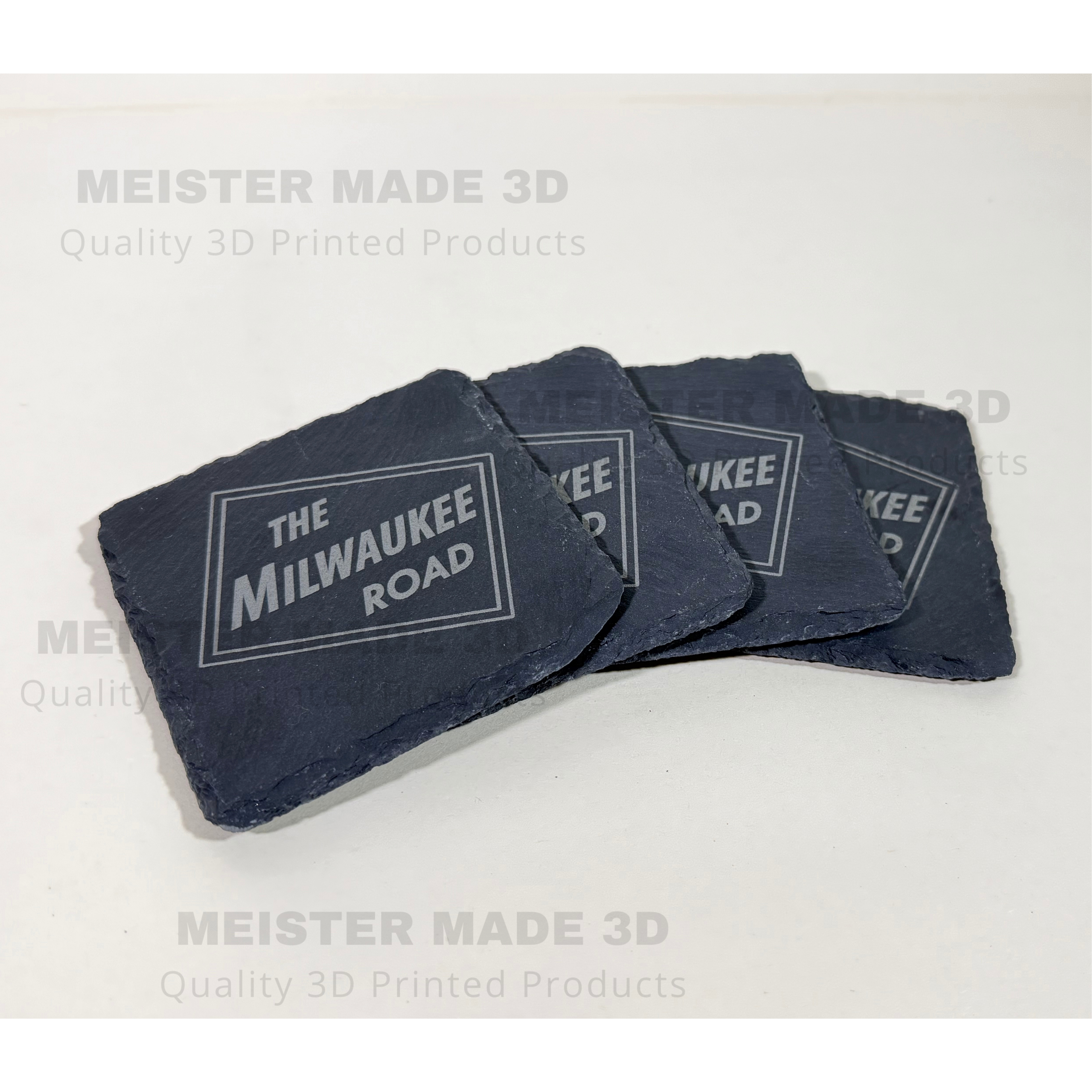 Four square dark slate coasters with a white printed 'THE MILWAUKEE ROAD' logo, arranged in a fan shape on a white background with 'MEISTER MADE 3D' watermarks.