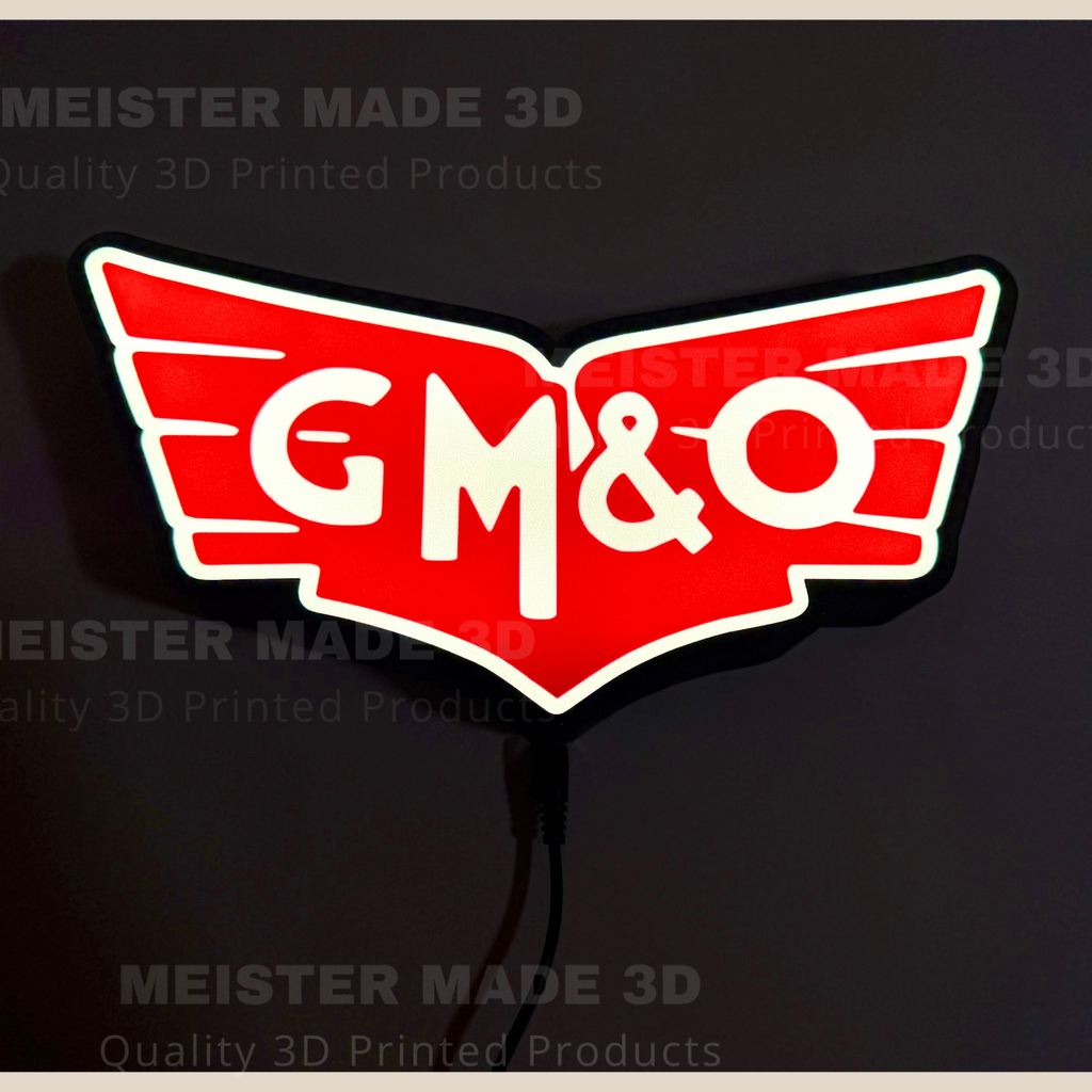 A 3D printed illuminated GM&O sign with a red winged emblem, white lettering, and a black backing, shown against a dark background with a power cord visible.