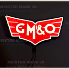 A 3D printed illuminated GM&O sign with a red winged emblem, white lettering, and a black backing, shown against a dark background with a power cord visible.