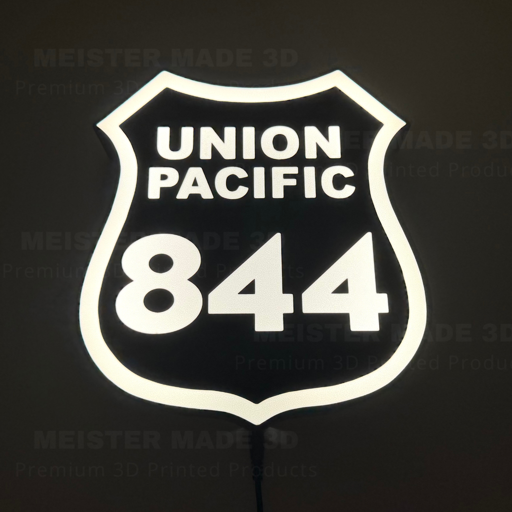 Glowing Union Pacific 844 railroad shield sign illuminated against a dark background, featuring bright white lettering and border with a black center.