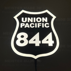 Glowing Union Pacific 844 railroad shield sign illuminated against a dark background, featuring bright white lettering and border with a black center.