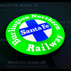 A circular 3D-printed illuminated sign for the Burlington Northern Santa Fe Railway, featuring a bright green outer ring with white lettering, a blue and white cross in the center, and the words 'Santa Fe' in white. The sign is photographed against a dark background with faint watermarks.